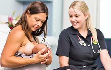 Woman breastfeeding baby with midwife